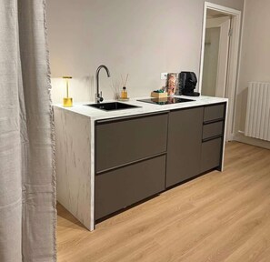 Une cuisine moderne avec un plan de travail blanc, des meubles de couleur sombre et un évier noir.