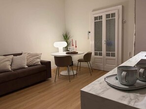 Un salon comprenant un canapé, une table ronde, deux chaises, une lampe et une porte dotée de panneaux en verre dépoli.