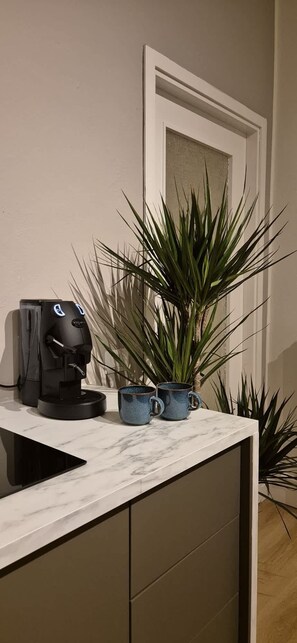 Une machine à café, deux tasses et une plante en pot, le tout posé sur un comptoir.