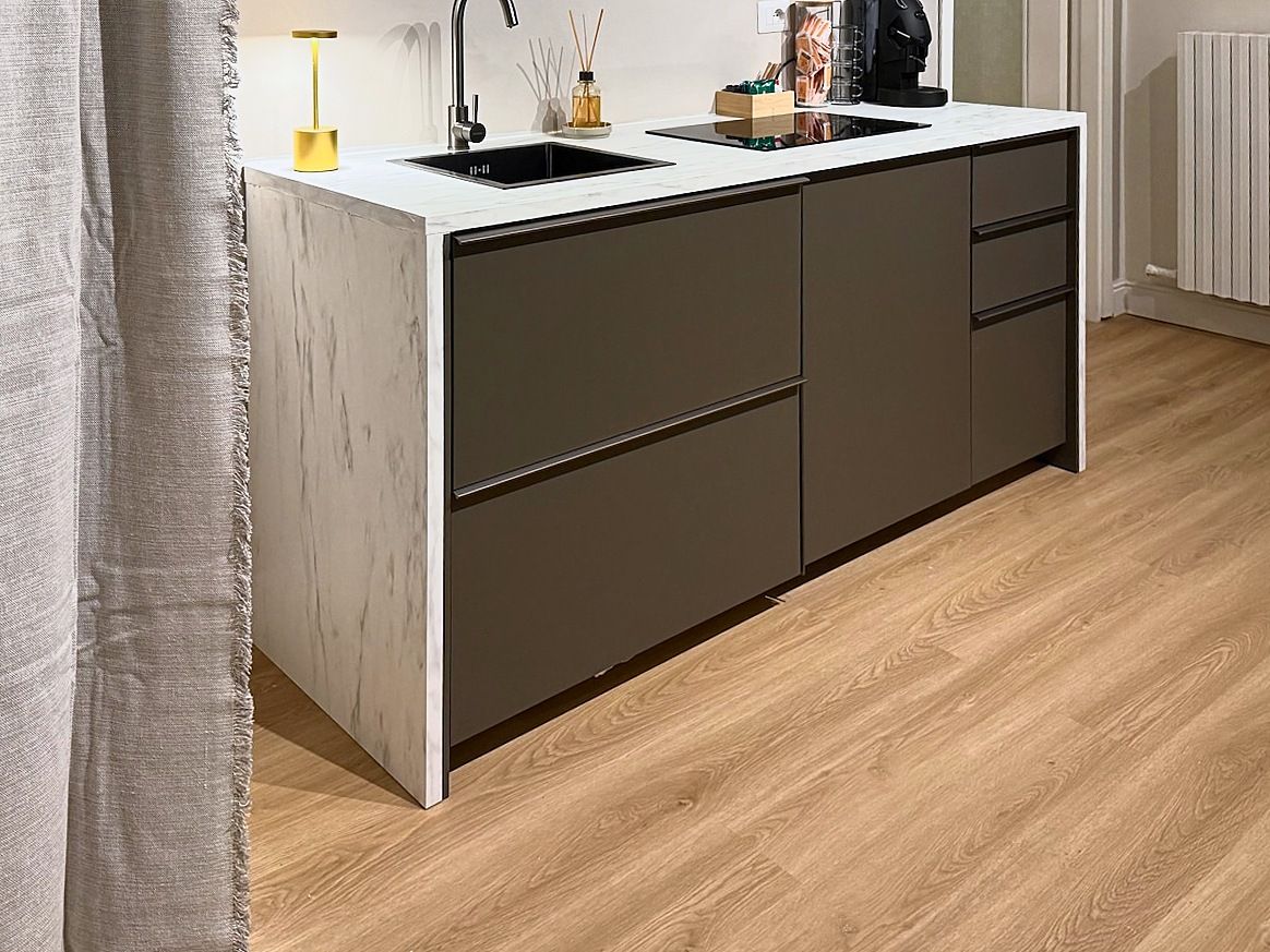Eine moderne Küche mit weißer Arbeitsplatte, dunklen Schränken und Holzboden.