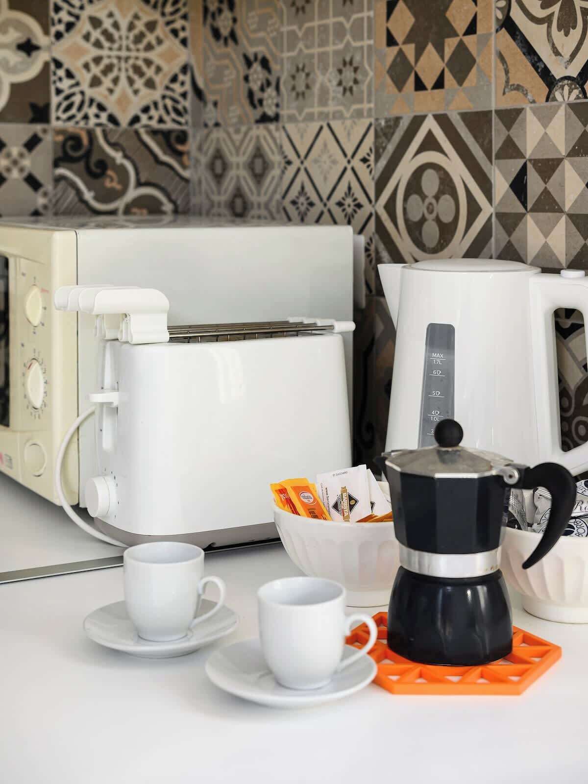 Cuina amb una torradora blanca, una cafetera negra i dues tasses blanques sobre una superfície de cuina blanca.