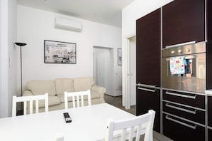 Une cuisine moderne dotée d’un four encastré et d’un coin repas avec une table et des chaises blanches.