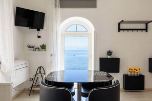 Ein modernes Zimmer mit einem runden Tisch, einem Flachbildfernseher, Meerblick durch einen Rundbogen und einer kleinen Ablage mit Pflanzen.