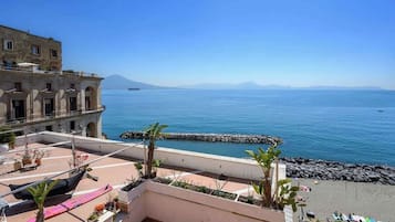 Une terrasse sur le toit offrant une vue sur la mer, un bâtiment orné d’arcades et une côte rocheuse.