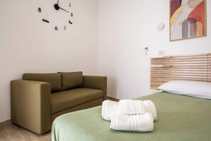 Een kamer met een bruine bank, een bed met een groen dekbed en een wandklok.