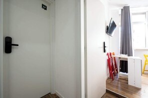 A room with a white door, a television mounted on the wall, a desk with a chair, and a window with curtains. - Standard · private kitchen & bath · Centrale (Naples)