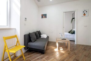 A modern living room with a grey sofa, a yellow folding chair, a small wooden table, and a painting on the wall. - Standard · private kitchen & bath · Centrale (Naples)