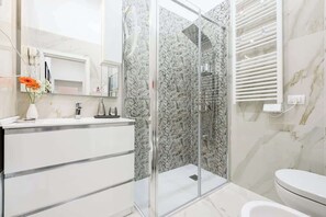 A modern bathroom with a glass-enclosed shower, a white vanity, and a marble-tiled wall. - 6Centrale at the Main Station (Naples)