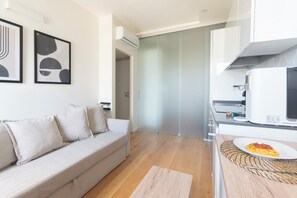 A modern living room with a sofa, a dining table with a plate of food, and a kitchen area with a microwave. - Between Central Station & Porta Nuova - 1 bedroom (Milan)