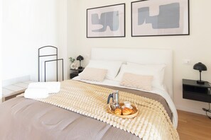 Ein ordentlich bezogenes Bett mit weißer Daunendecke, einer braunen Tagesdecke und einem Korb mit Croissants auf dem Bett.