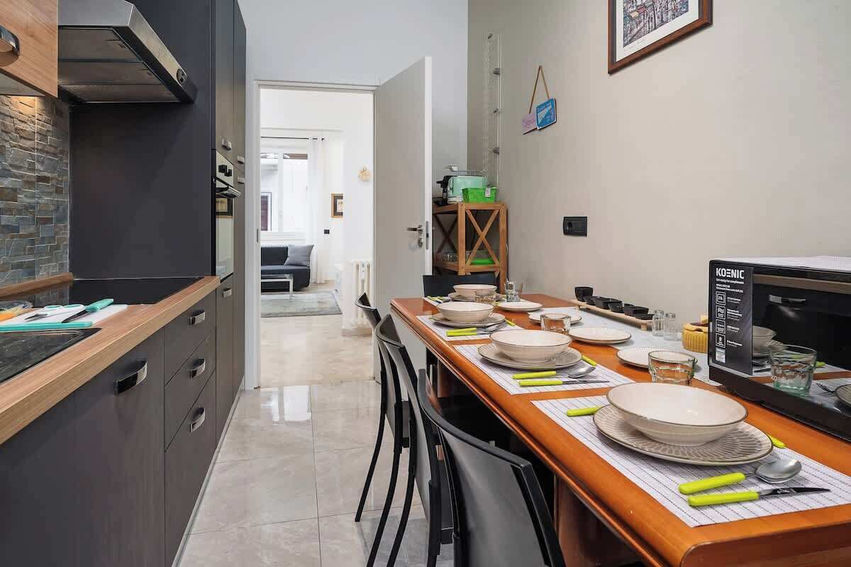 A modern kitchen with a dining area, featuring a kitchen island, a built-in oven, and a dining table set with plates and cutlery.