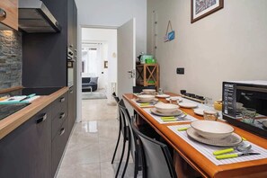 A modern kitchen with a dining area, featuring a kitchen island, a built-in oven, and a dining table set with plates and cutlery. - Vicino Malpensa, Tribunale e Ospedale @Busto (Busto Arsizio)
