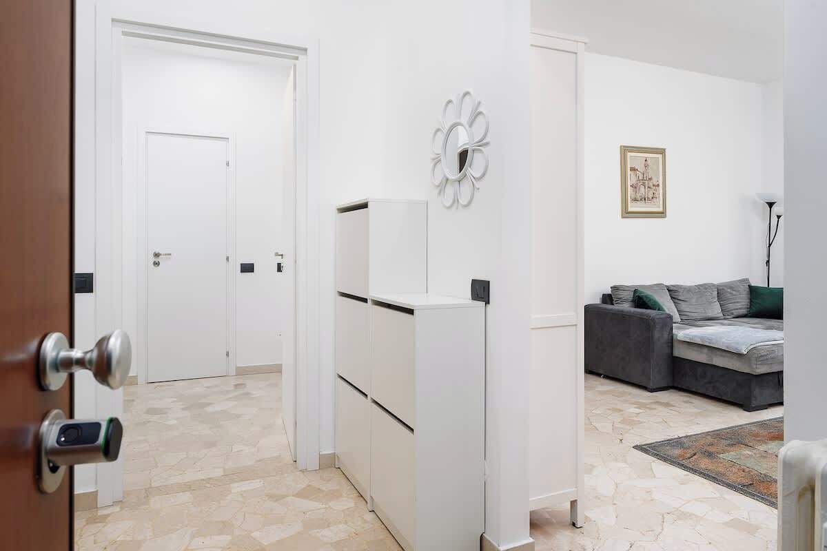 Un intérieur moderne avec une porte blanche, un meuble blanc, un canapé gris et un tapis à motifs.