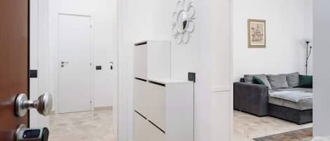 A modern interior with a white door, a white cabinet, a grey sofa, and a patterned rug.