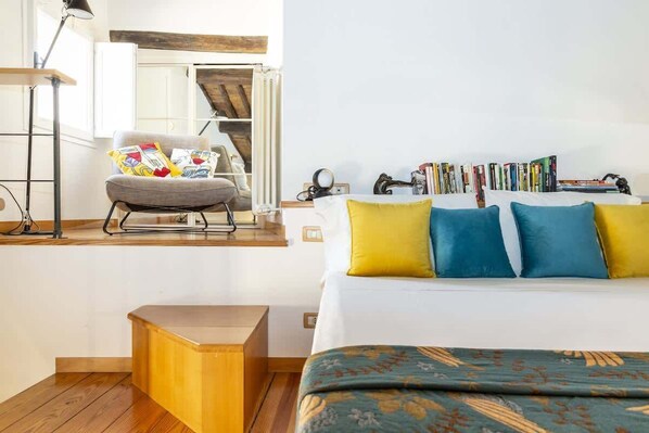 A bedroom with a bed, a chair, a small wooden table, and a bookshelf. - Monti - Stunning Loft in the Heart of Rome's Monti (Rome)