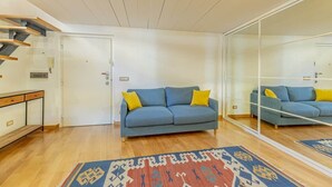 Een woonkamer met een bank, een kamerbreed tapijt, een houten bankje en een glazen scheidingswand.