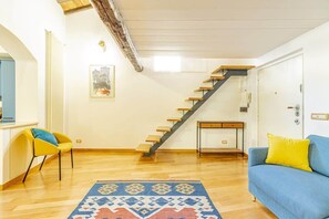 A living room with a staircase, a sofa, a chair, and a patterned rug. - Monti - Stunning Loft in the Heart of Rome's Monti (Rome)