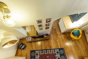 A room with a wooden floor, a patterned rug, a yellow chair, and wall-mounted artwork. - Monti - Stunning Loft in the Heart of Rome's Monti (Rome)