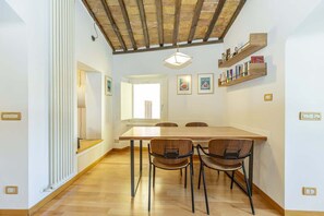 A dining area with a wooden table and chairs, a ceiling with exposed beams, and wall-mounted shelves with books. - Monti - Stunning Loft in the Heart of Rome's Monti (Rome)