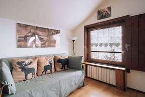 Un salón con sofá, arte en la pared, un radiador y una ventana decorada con motivos de corazón.