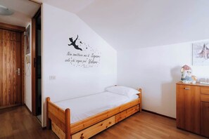 Un dormitorio con una cama de madera, un adhesivo en la pared y un pequeño mueble con un oso de peluche.