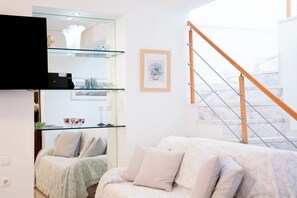 A living room with a sofa, a glass shelf unit, a framed picture, and a staircase. - Premium Penthouse with Stunning Views and Free Gated Parking next to Metro (Μενεμένη)