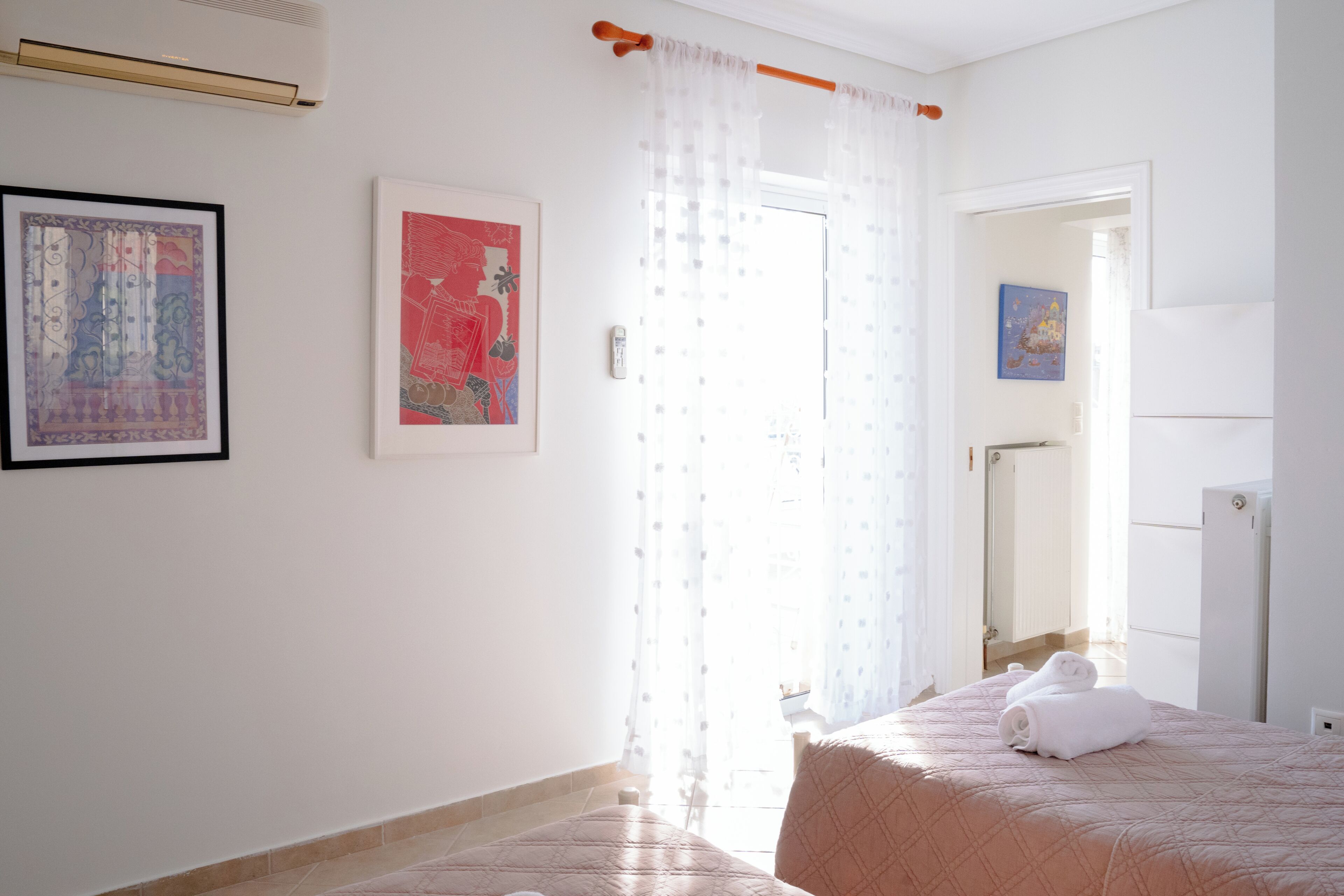 A bedroom with a bed, a window with curtains, a door, and a wall-mounted air conditioner.
