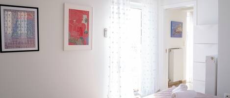 A bedroom with a bed, a window with curtains, a door, and a wall-mounted air conditioner.