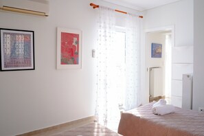 A bedroom with a bed, a window with curtains, a door, and a wall-mounted air conditioner. - Premium Penthouse with Stunning Views and Free Gated Parking next to Metro (Μενεμένη)