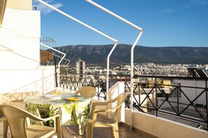 A terrace with a table and chairs, overlooking a cityscape and mountains. - Premium Penthouse with Stunning Views and Free Gated Parking next to Metro (Μενεμένη)