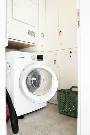 A front-loading washing machine in a laundry room with a green laundry basket and numbered storage cabinets. - Premium Penthouse with Stunning Views and Free Gated Parking next to Metro (Μενεμένη)
