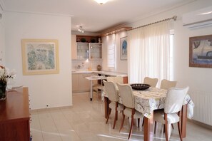 A dining area with a table set for four, surrounded by chairs. There is a kitchen in the background with cabinets and a window. - Premium Penthouse with Stunning Views and Free Gated Parking next to Metro (Μενεμένη)