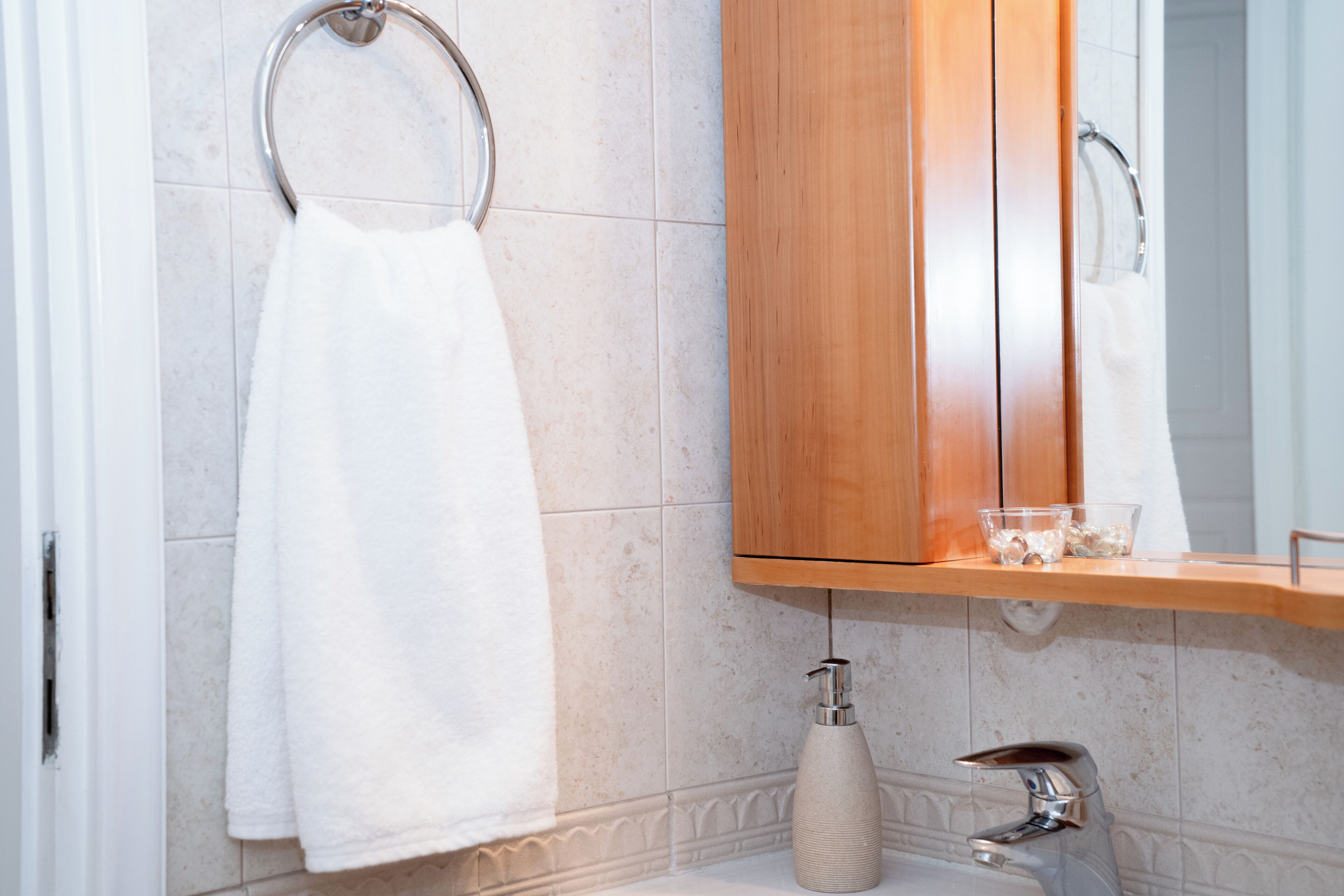 A bathroom with a wooden vanity, a towel rack, a soap dispenser, and a mirror.
