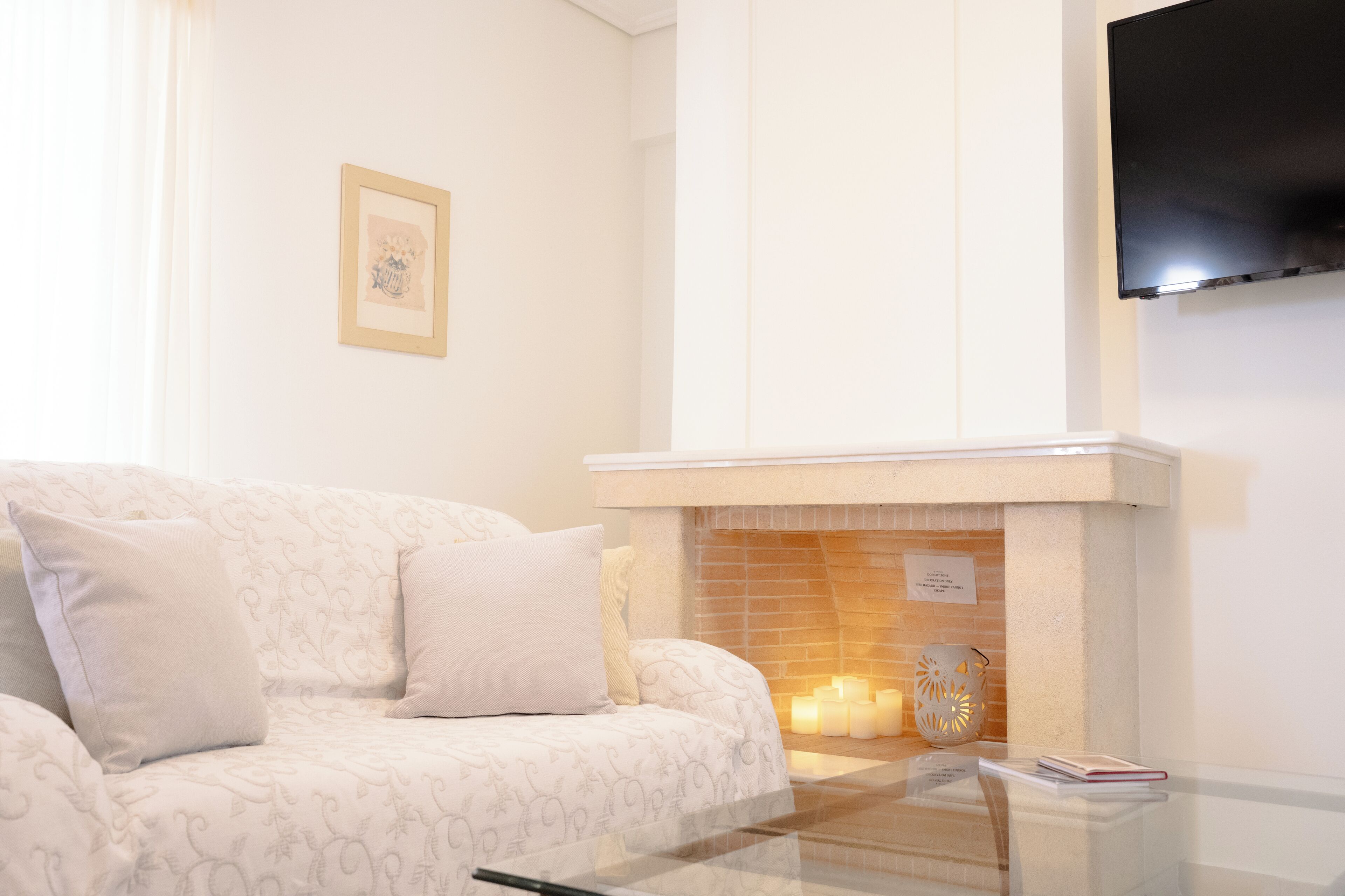 Un salon comprenant un canapé, une cheminée, un téléviseur à écran plat fixé au mur et une table basse en verre.