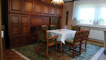 Ein Esszimmer mit Holzschrank, Tisch und Stühlen sowie einem fensterförmigen Bereich mit Vorhängen.