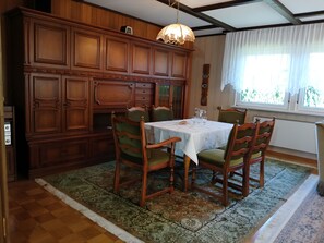 Een eetkamer met een houten kast, een tafel met stoelen en een raam met gordijnen.