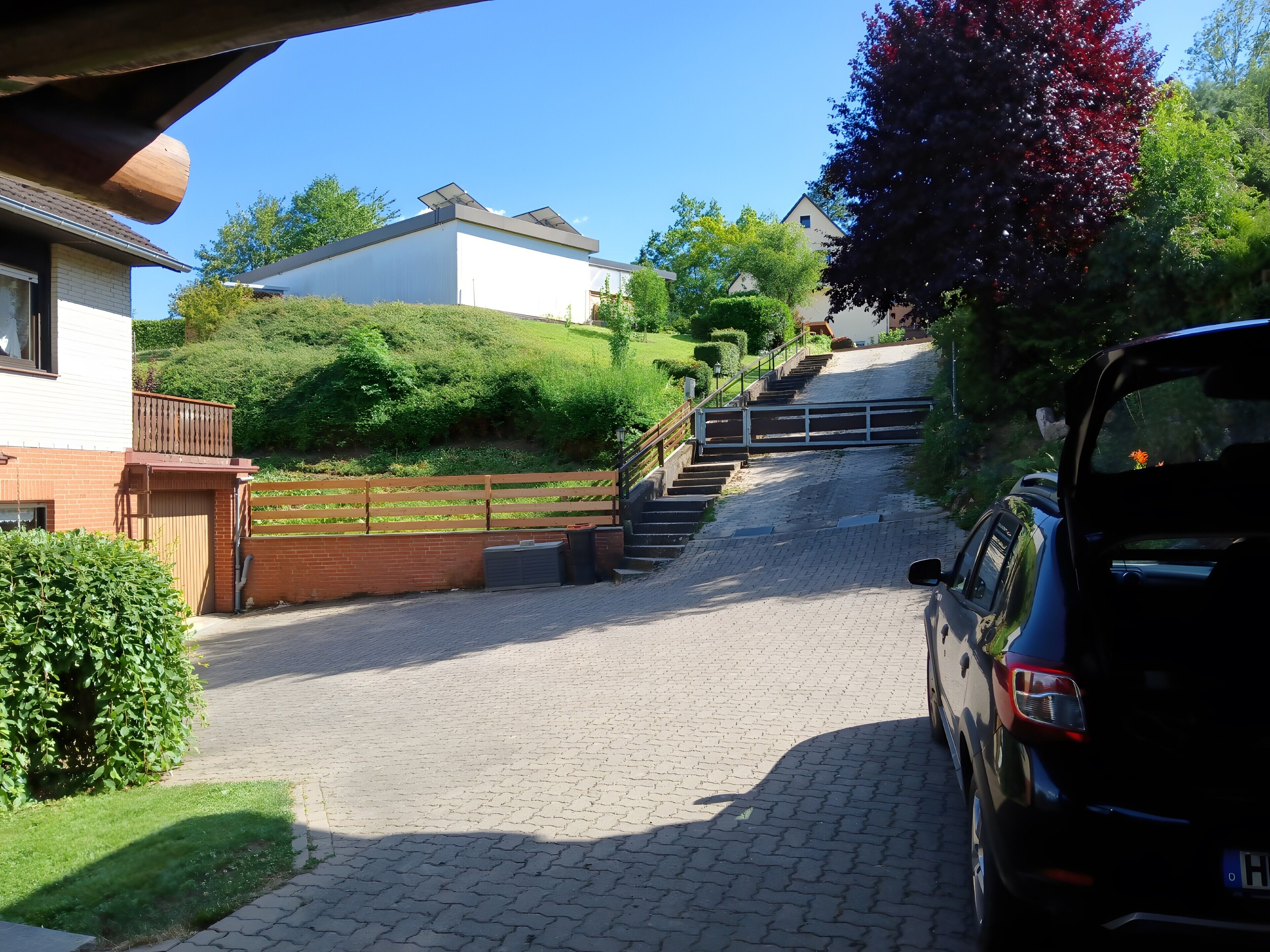 A paved driveway leading to a house with a wooden fence and a car parked on the right.