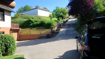 A paved driveway leading to a house with a wooden fence and a car parked on the right.