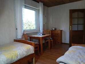 Una habitació amb dos llits de fusta, una taula de fusta i cadires, un armari i una finestra amb cortines.