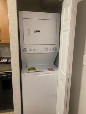 Un appareil compact combinant lave-linge et sèche-linge, installé dans une petite buanderie avec un meuble en bois et un lave-vaisselle.