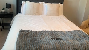 Un lit bien fait, avec une couverture bleue, une tête de lit sombre et deux panneaux décoratifs fixés au mur.