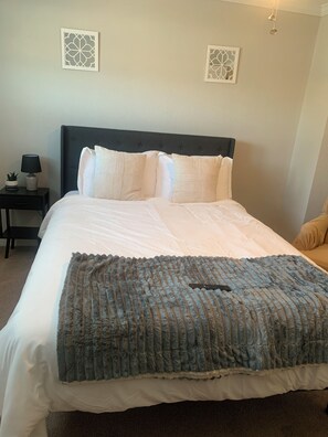A neatly made bed with a blue blanket, a dark headboard, and two wall-mounted decorative panels. - Better Days (Charlotte)