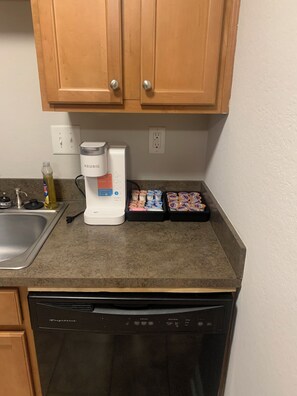 A kitchen with wooden cabinets, a coffee maker, a dish rack, and a dishwasher. - Better Days (Charlotte)