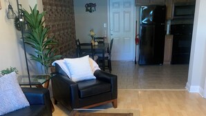 Un salon avec un canapé en cuir noir, une table basse en verre ornée d’une plante et d’une bougie, et un coin repas avec une table et des chaises.