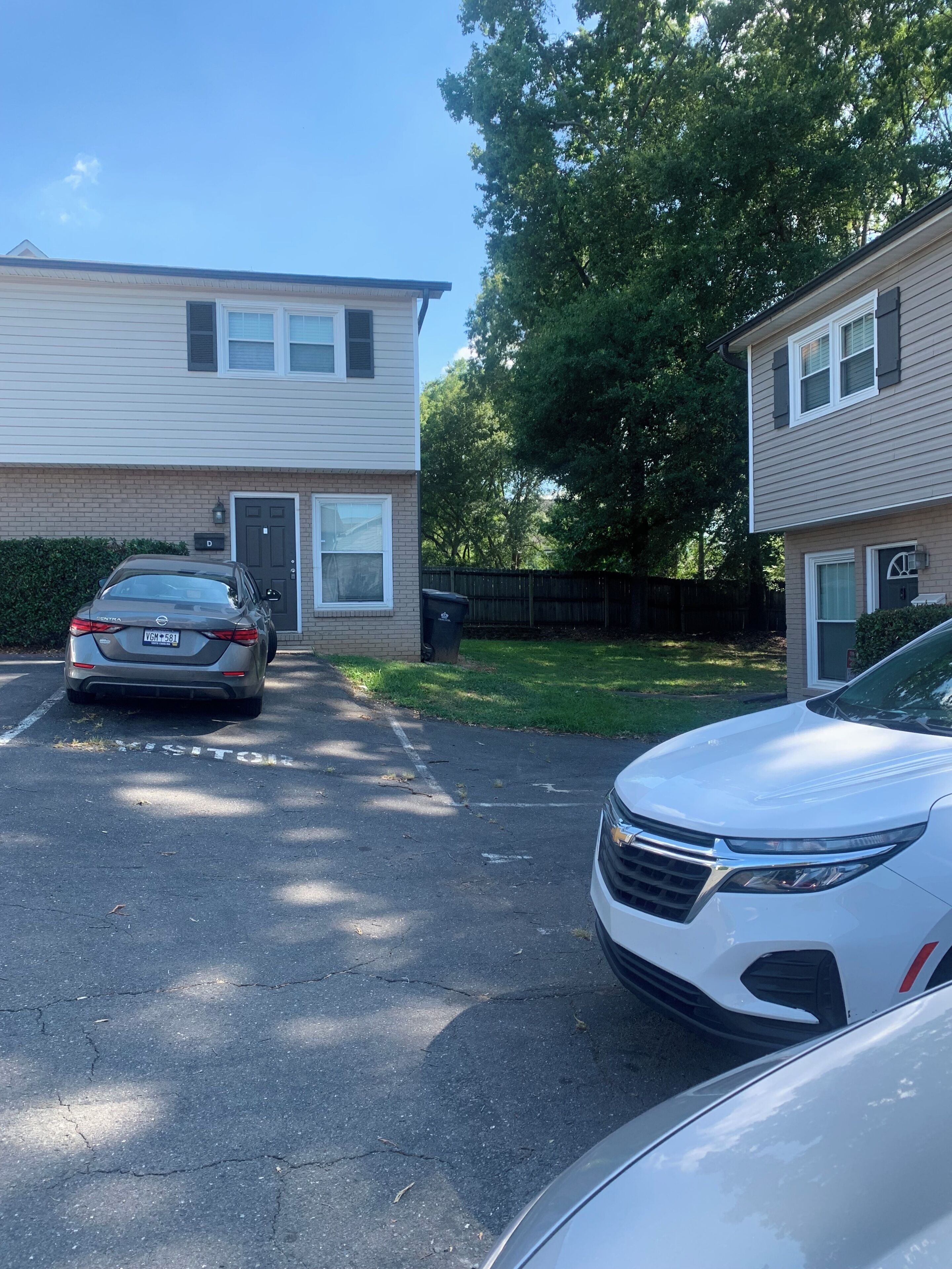 A residential street with two-story houses, a parking area, and a driveway.