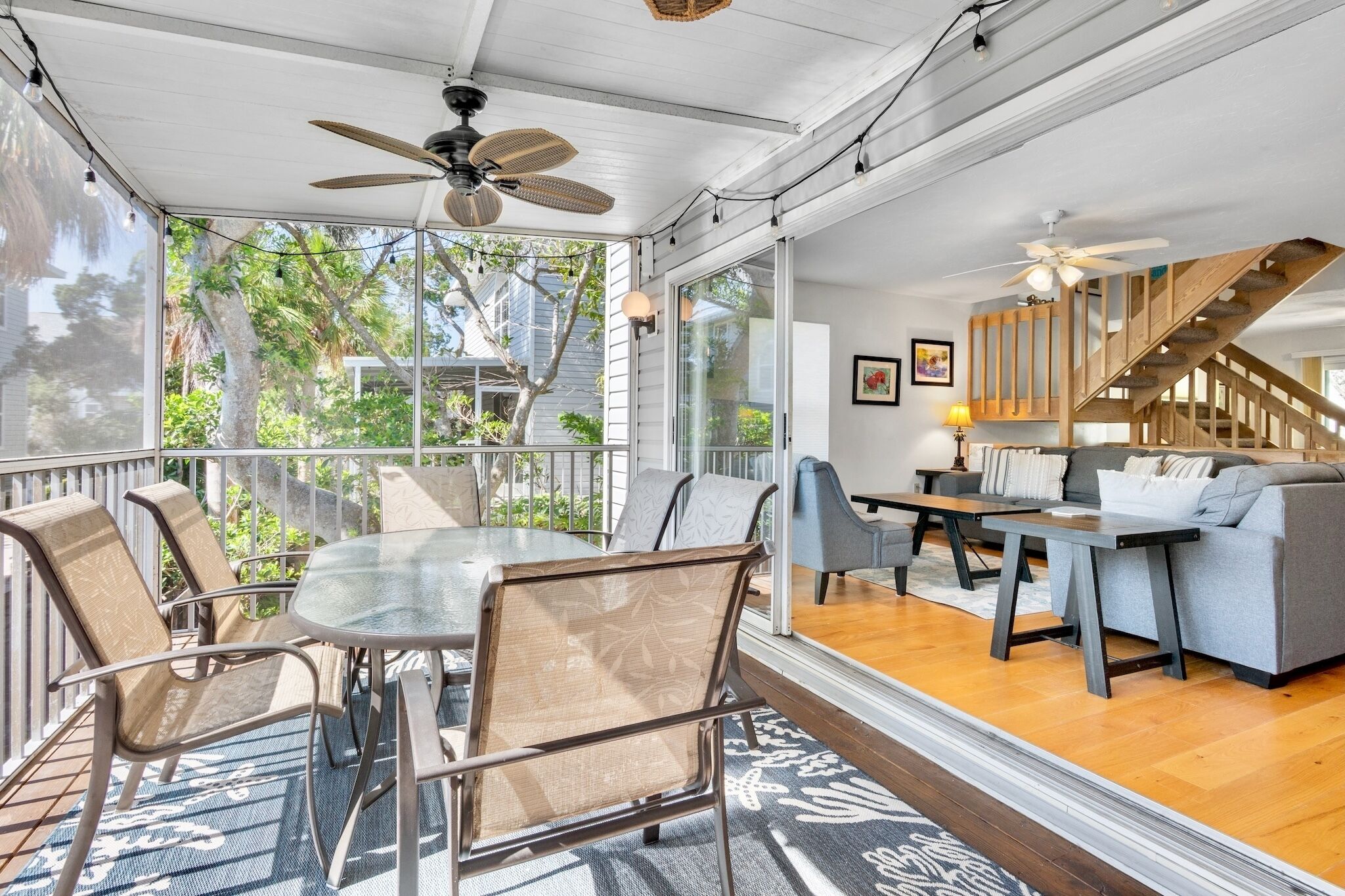 A covered patio with a dining table and chairs, a sofa, and a staircase leading to an upper level.
