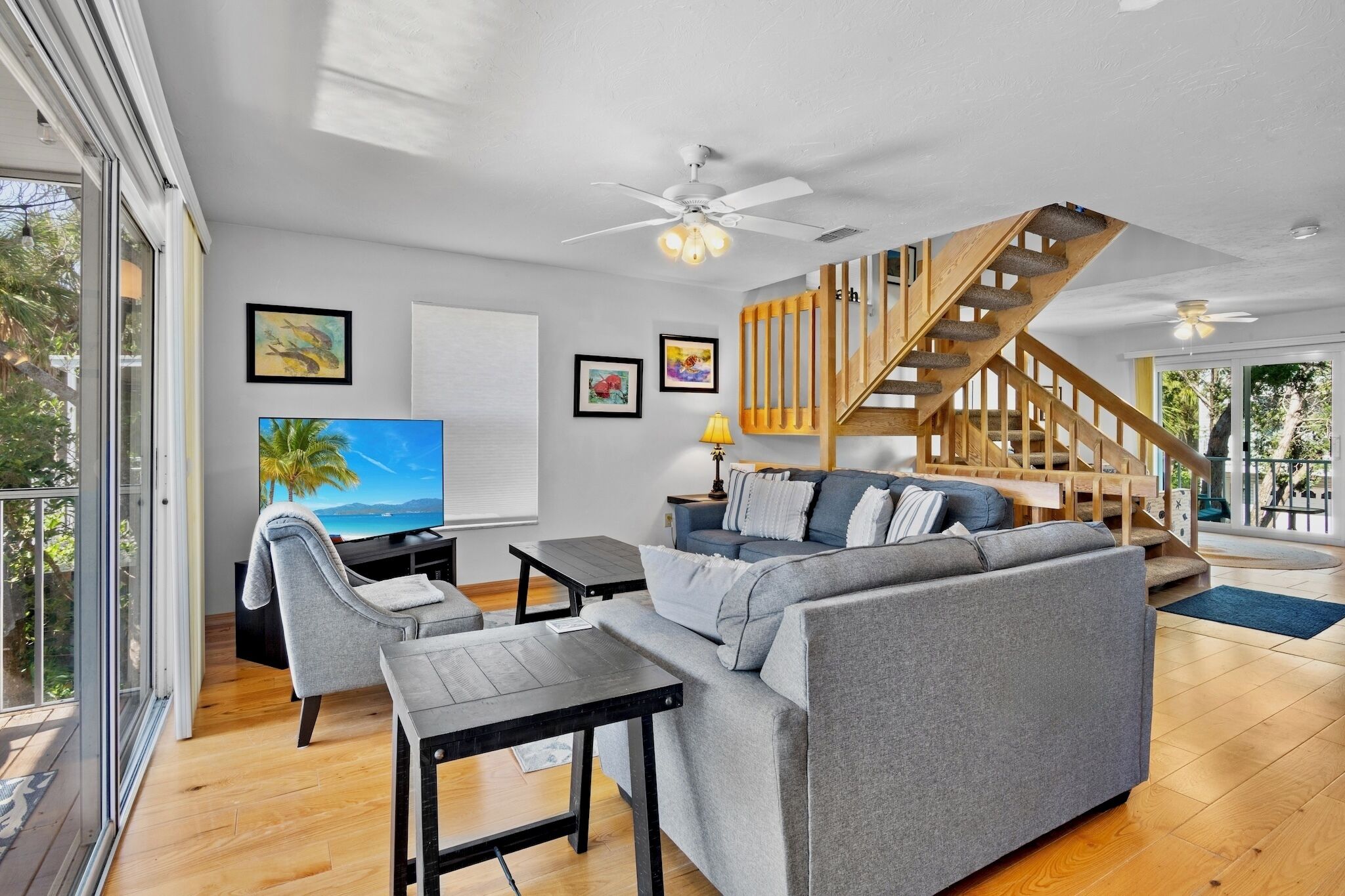 Ein modernes Wohnzimmer mit einem grauen Sofa, einem Fernseher, einer Holztreppe und einem Balkon mit Blick.