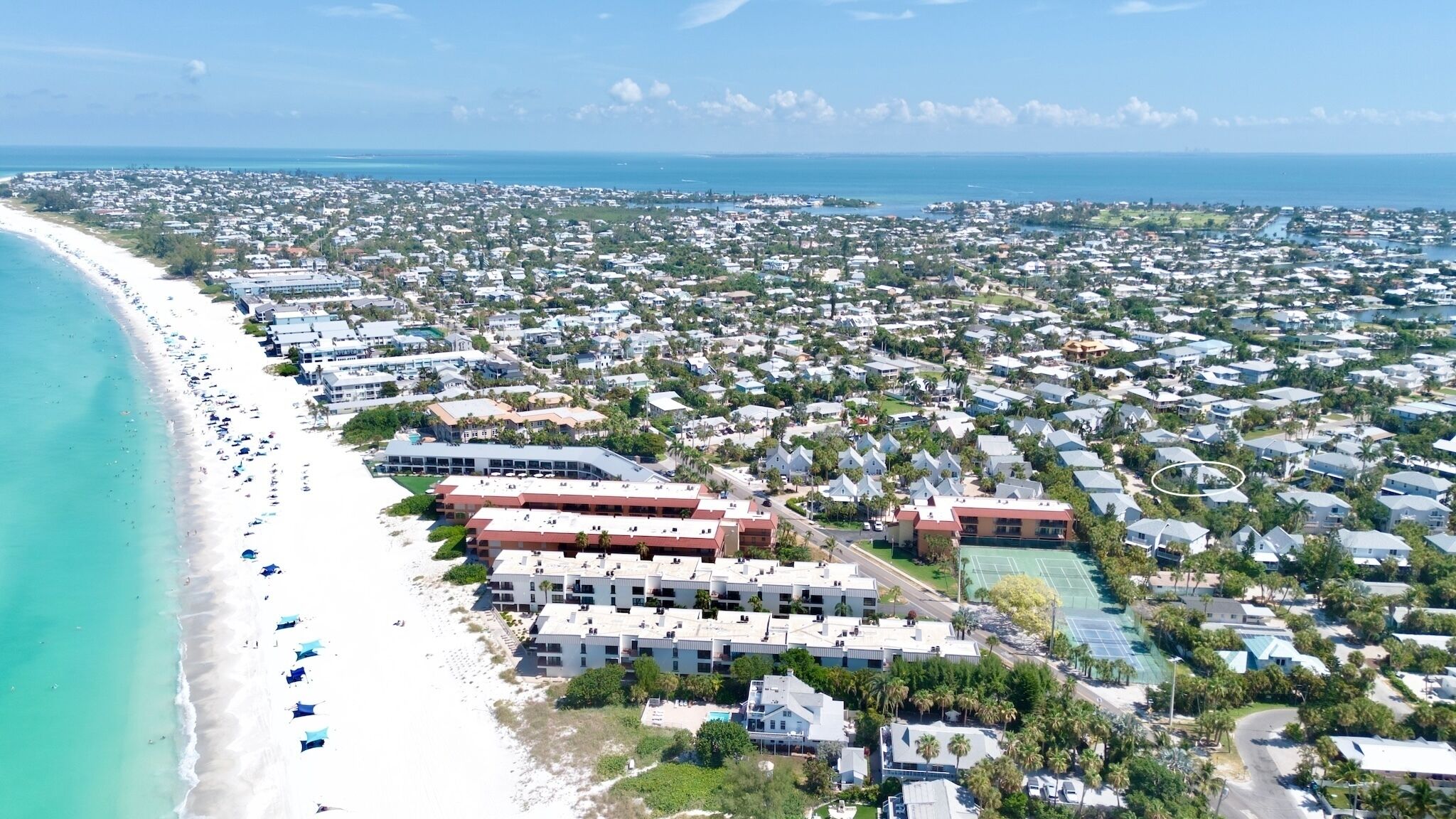 Een kustgebied met woonhuizen direct aan het strand, een groot complex en een tennisbaan.