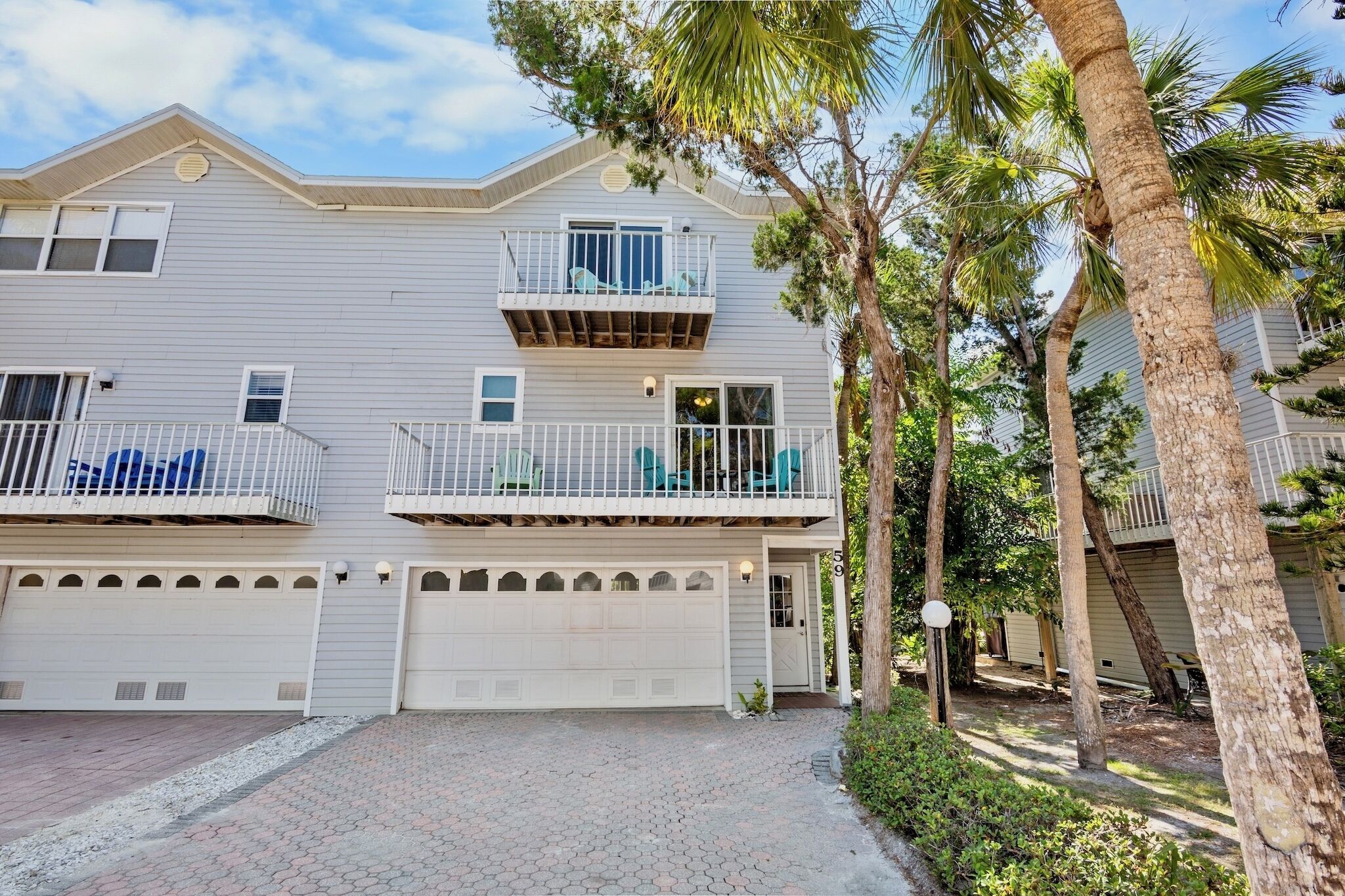 A two-story residential building with a garage, a balcony with chairs, and a driveway.