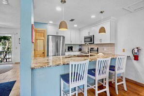 A modern kitchen with a central island, white cabinetry, stainless steel appliances, and pendant lighting. - Sunshine Daydream in Anna Maria Island (Holmes Beach)